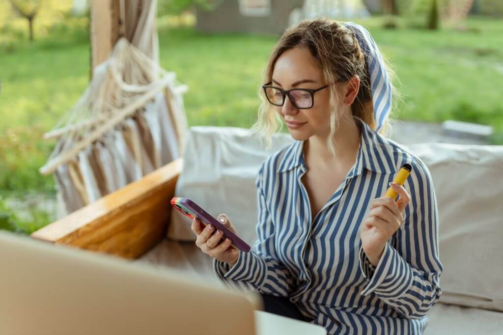 A beautiful girl smokes an electrode cigarette and uses a smartphone. Event Organizer